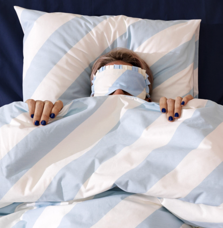 Image of a person covered up in IKEA blanket duvet and sleeping on a pillow cased with IKEA pillow cover, covering their eyes with IKEA blindfold, all having the same baby blue and white stiped pattern.